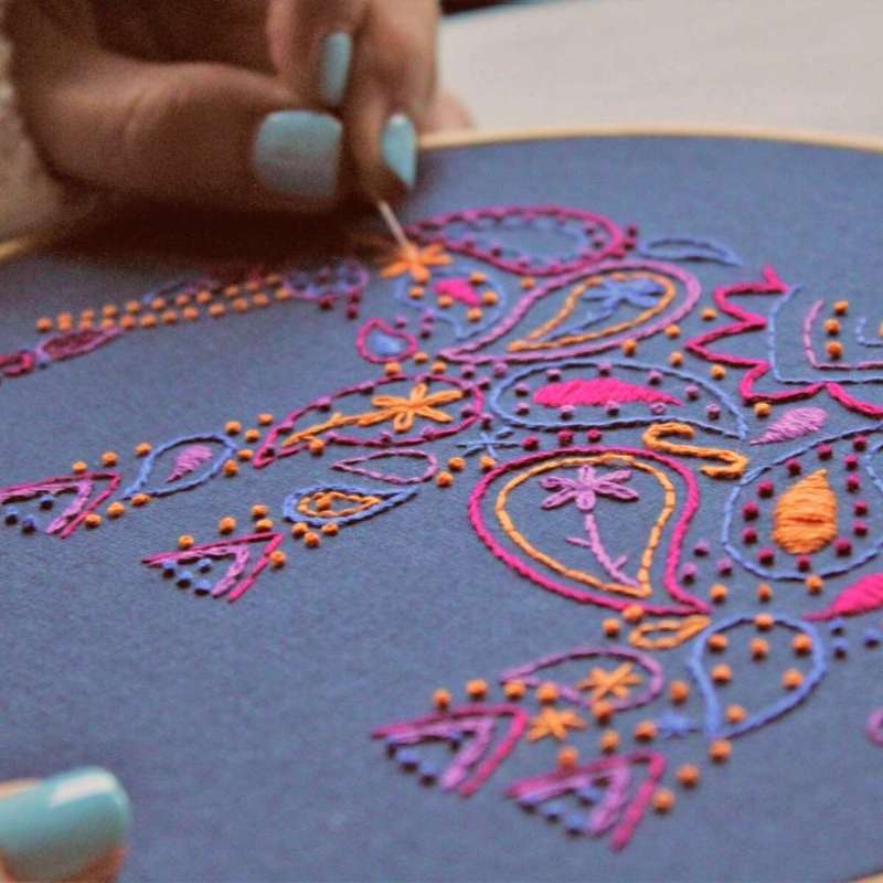 Purple, blue, red, lilac and orange elephant embroidery kit angled shot with hand holding needle