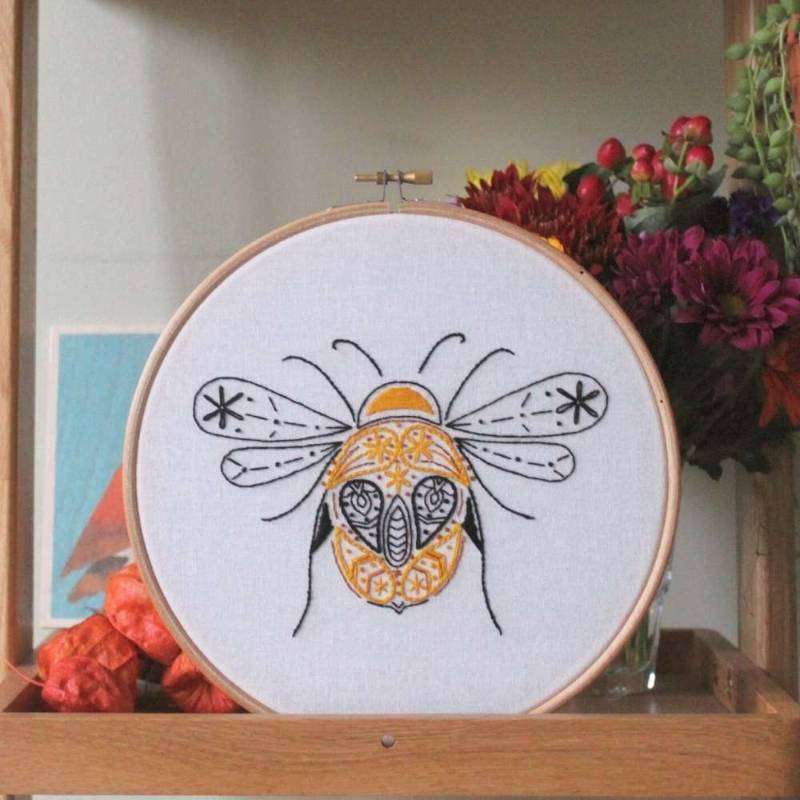 Bee embroidery kit on shelf with flowers behind 