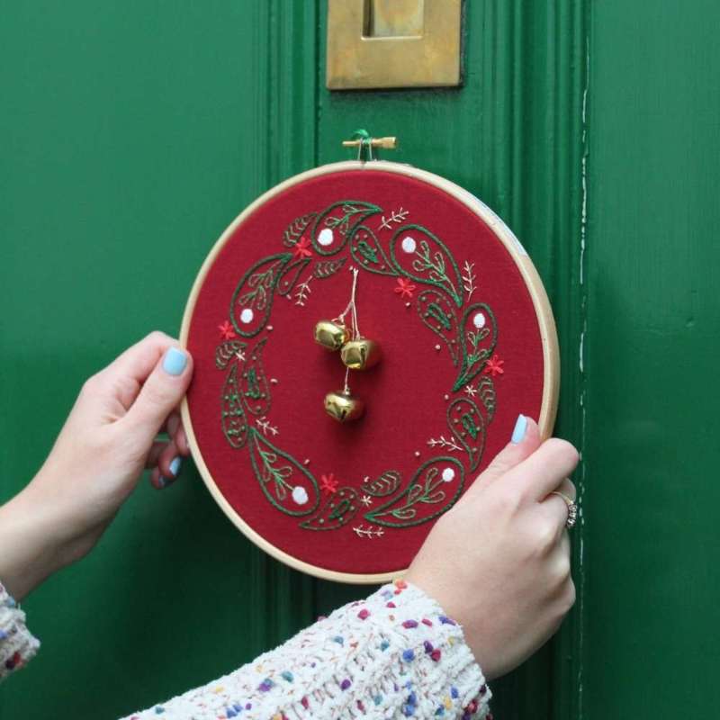 Embroidered christmas wreath held in hands with green door in background