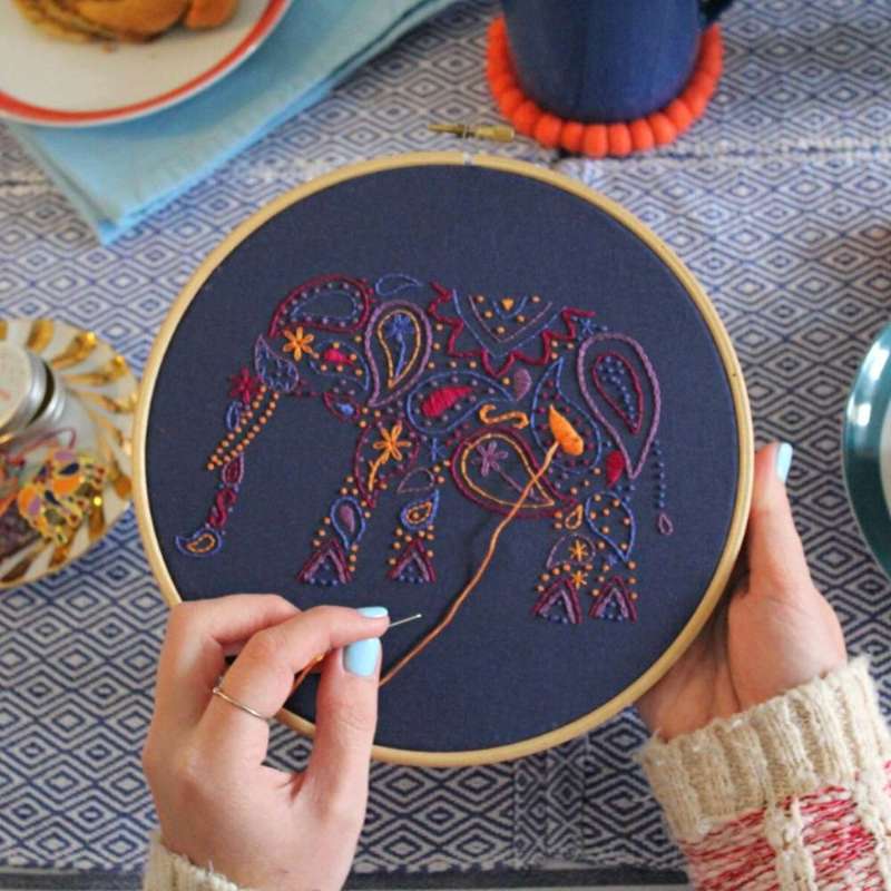 Purple, blue, red, lilac and orange elephant on  navy fabric being stitched by hands