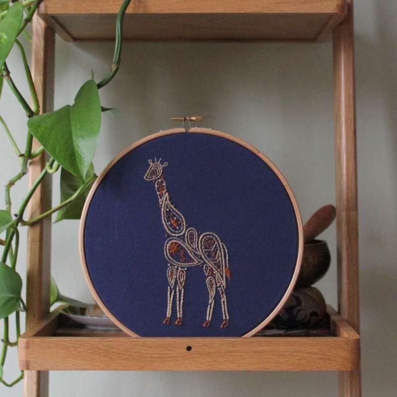 Paisley Giraffe embroidery piece in two shades of brown on navy fabric on shelf