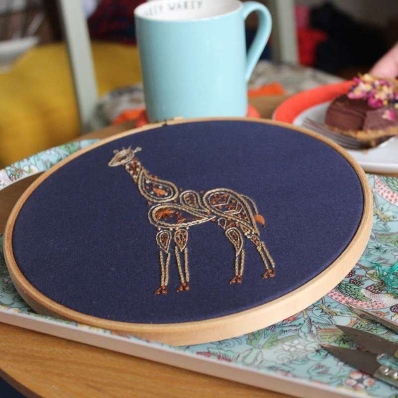 Angled photo of embroidered paisley giraffe in two shades of brown on navy fabric