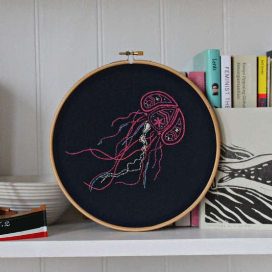 Pink silver and blue jellyfish embroidery design on navy fabric on shelf with ornaments