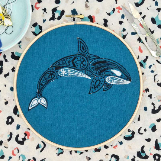 A black and white embroidered Orca on Teal fabric with ornaments in the background