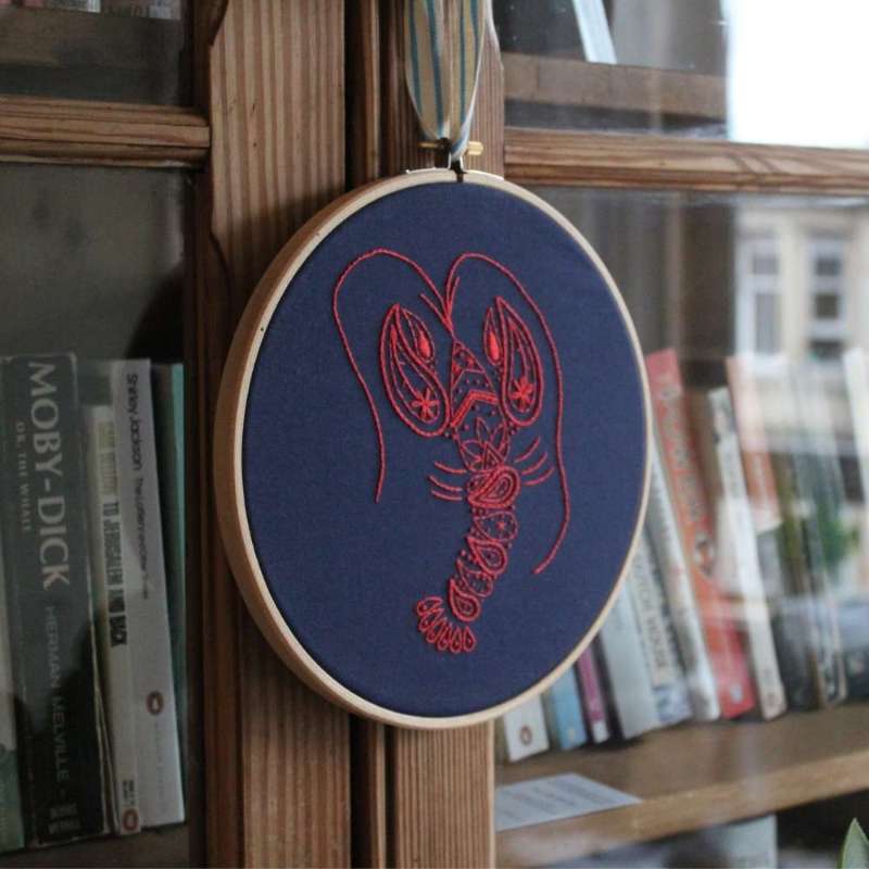 Red embroidered lobster on navy fabric hanging on a wooden bookshelf