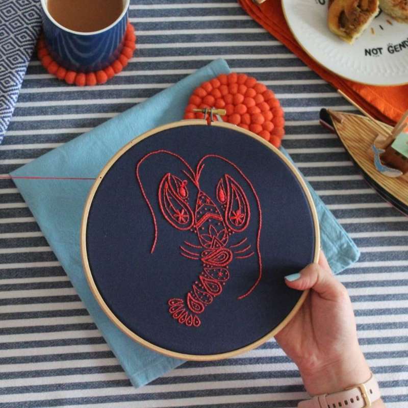 Red embroidered lobster on navy fabric in hoop with table and ornaments in background