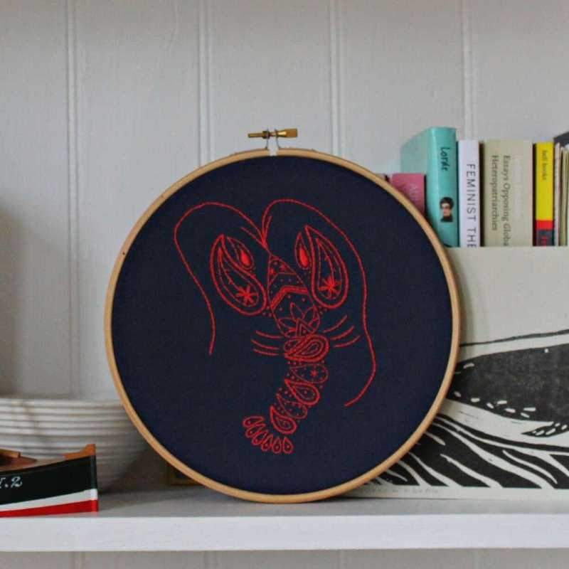 Red lobster embroidered on navy fabric rested in a wooden hoop on shelf