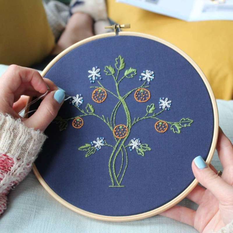 Green and white Orange tree embroidery kit in hands on navy fabric 