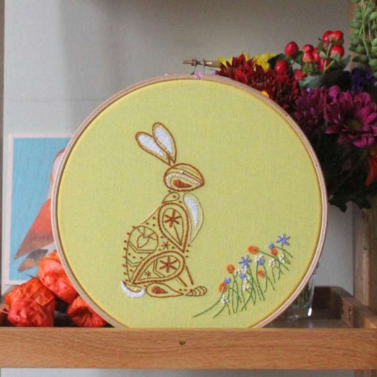 An embroidered brown and white paisley rabbit with orange white and purple flowers sewn on a yellow fabric