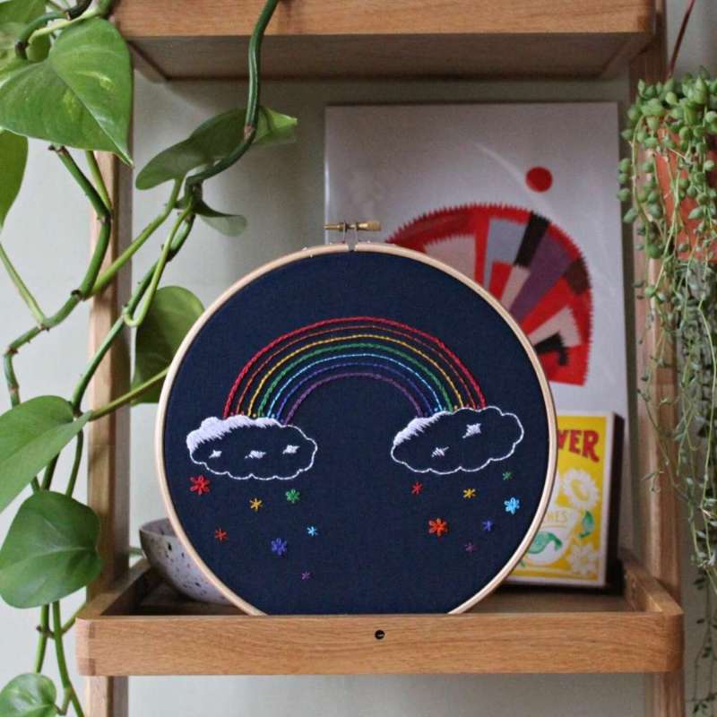 A completed rainbow embroidery kit in a hoop resting on a shelf with plants