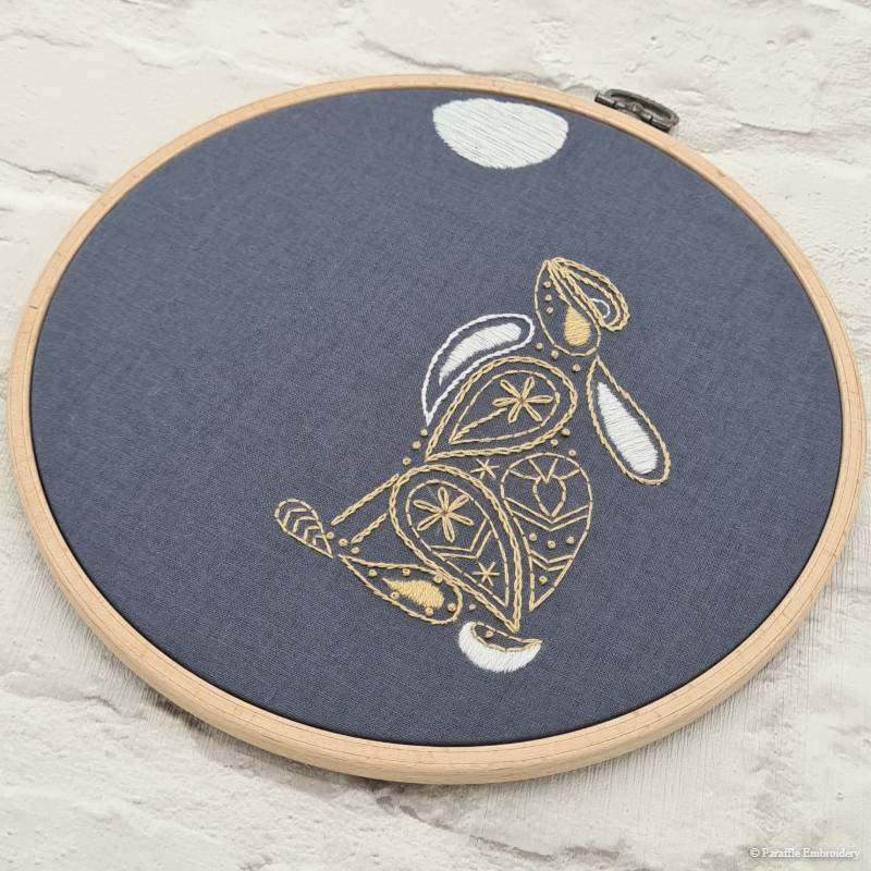 Angled picture of hare embroidery on grey fabric in wooden hoop