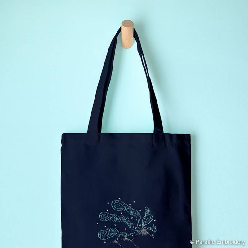 Lifestyle view of paisley northern lights embroidery on navy tote hanging from hook