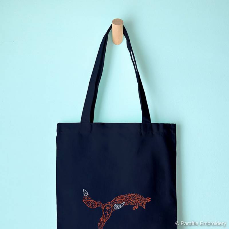 Lifestyle view of paisley fox hand embroidery on navy tote hanging on a hook