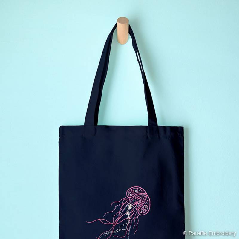 Lifestyle picture of paisley jellyfish embroidery on navy tote bag hanging from hook