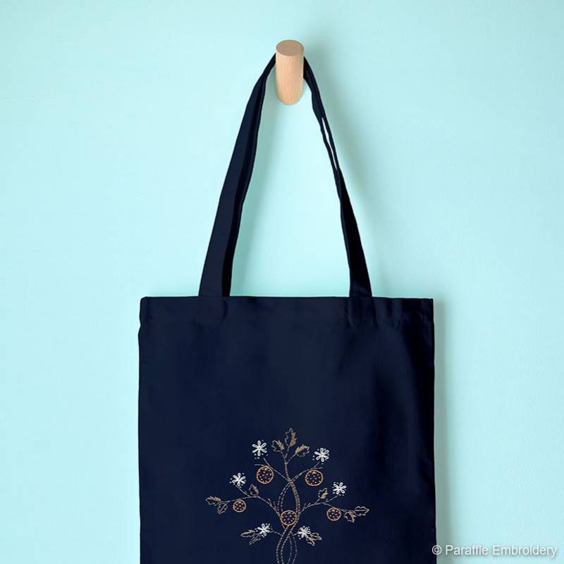 Lifestyle view of paisley orange tree embroidery on navy tote hung from hook